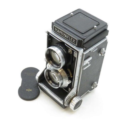 Twin-lens reflex camera with "Mamiyaflex" branding, featuring silver and black details, next to a lens cap.