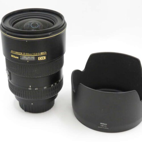 A Nikon DX 17-55mm f/2.8 camera lens with a separate lens hood placed beside it.
