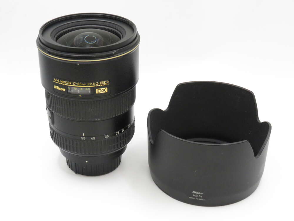 IMG_3644 A Nikon DX 17-55mm f/2.8 camera lens with a separate lens hood placed beside it.