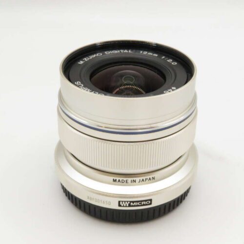 Silver Olympus M.Zuiko Digital 12mm f/2.0 lens on a white background, marked "Made in Japan."