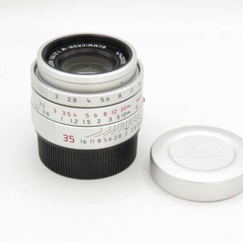 A white camera lens with numeric aperture markings sits next to its detached cap on a white background.