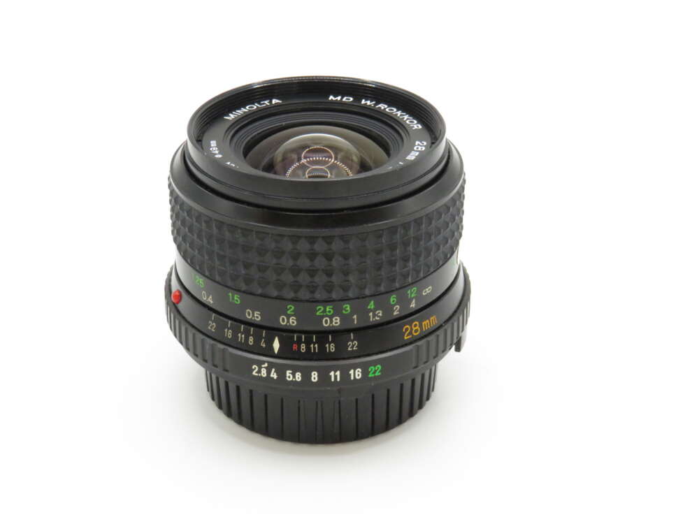 IMG_3762 A vintage Minolta camera lens with a textured grip, marked with various focal lengths and aperture values, stands against a plain white background.
