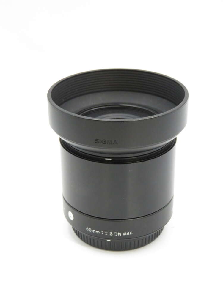 IMG_3856 A black Sigma 60mm f/2.8 DN lens with a textured focus ring and lens hood.