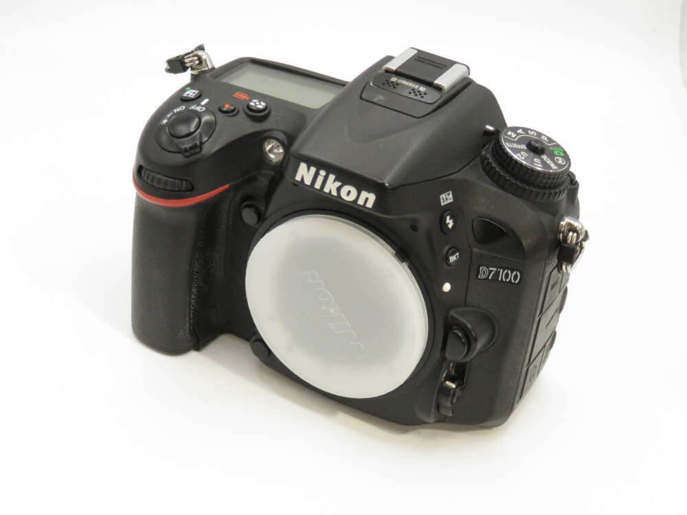 IMG_3862 Nikon D7100 DSLR camera with a body cap, featuring a control dial and textured grip against a white background.