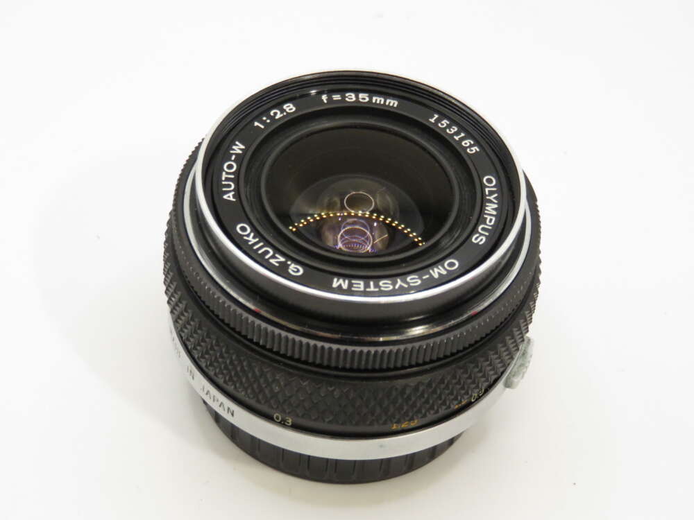 IMG_3893 A vintage Olympus camera lens with 35mm focal length and f/2.8 aperture, shown from the front.