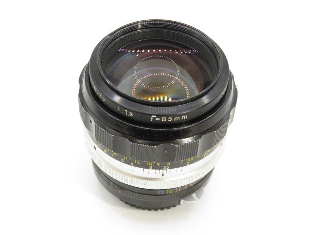 IMG_3899 A camera lens with f/1.8 and focal length of 85mm, featuring a silver and black design with visible aperture and focus rings.