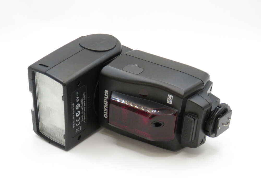 IMG_3949 Black Olympus camera flash unit lying on its side on a white surface.