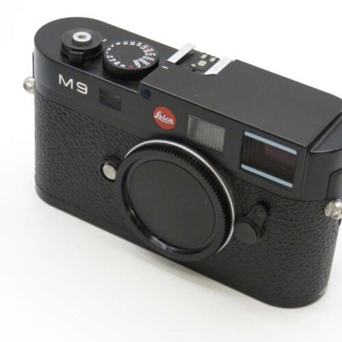 A black Leica M9 camera with a lens cap, showing a prominent red Leica logo and control dials on top.