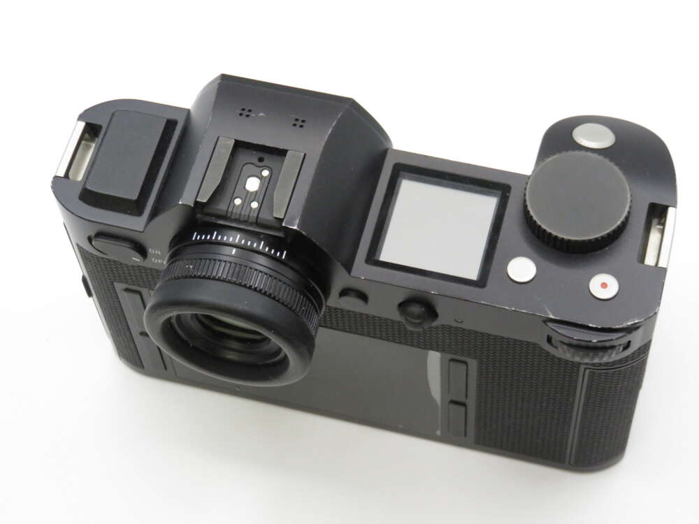 Black digital camera viewed from the top with a small LCD screen and several buttons.
