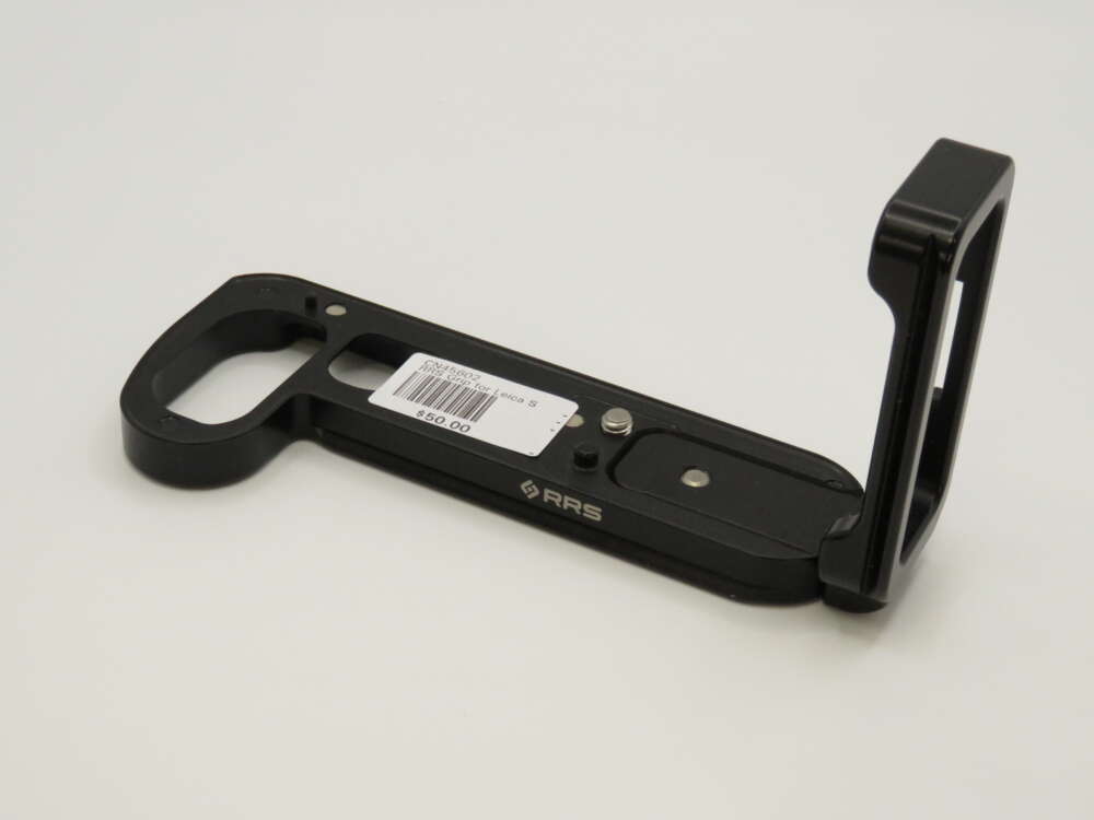 IMG_3998 A black L-bracket with a barcode sticker and mounting holes, designed for camera attachment, placed on a plain surface.