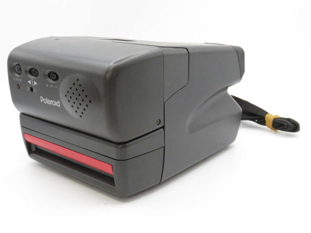IMG_4071 A vintage Polaroid instant camera with a dark grey body and a red film slot, featuring a carrying strap.