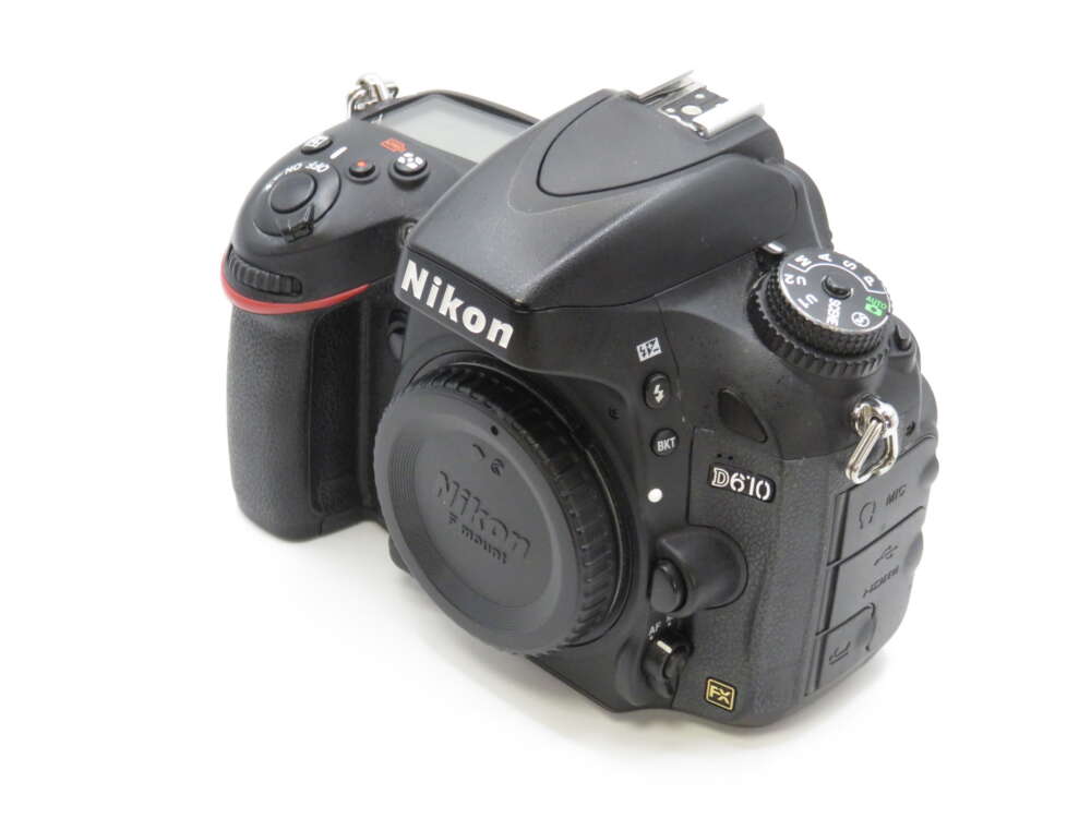 IMG_4133 A Nikon D610 DSLR camera with a lens cap on, showing several buttons, dials, and its logo.