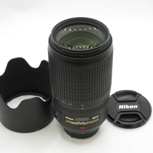 A Nikon zoom lens with a lens hood and cap resting on a white surface.