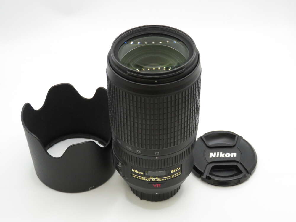 IMG_4141 A Nikon zoom lens with a lens hood and cap resting on a white surface.
