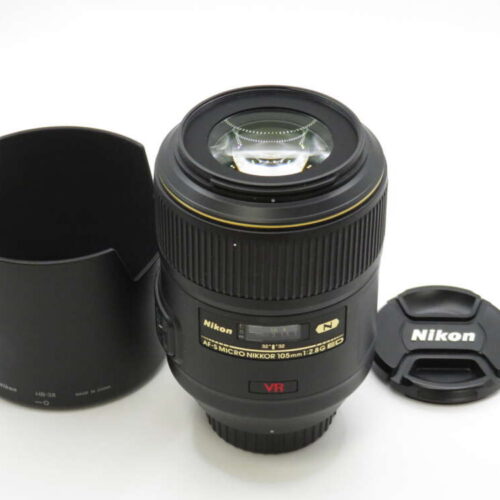 Nikon camera lens with VR feature, lens cap, and lens hood on a white surface.