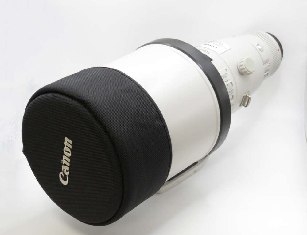 A large white Canon camera lens with a black protective cover displaying the Canon logo.