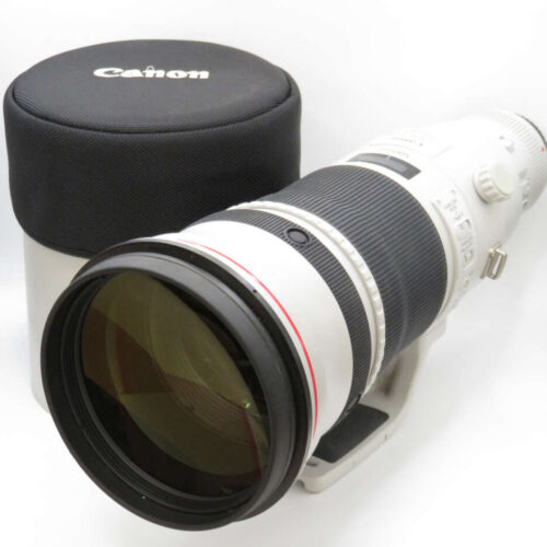 A white Canon telephoto lens with a black padded case beside it.