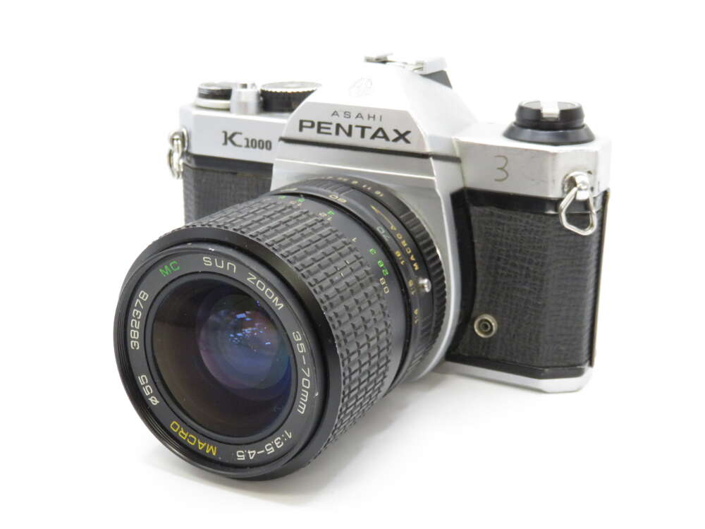 IMG_4193 A vintage Asahi Pentax K1000 camera with a Sun Zoom lens is shown on a white background.