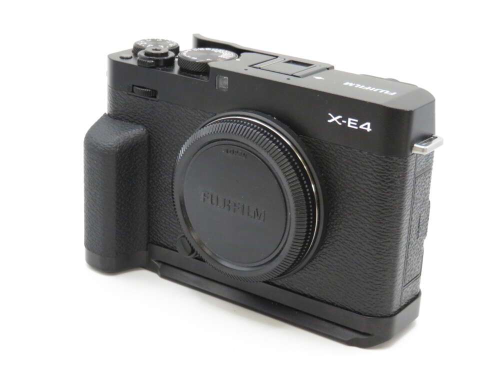 IMG_4205 A black Fujifilm X-E4 camera with a textured grip and visible dials, viewed from a front angle with the lens cap on.