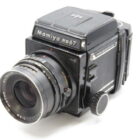 A vintage Mamiya RB67 medium format camera with a large lens and visible brand markings on a plain background.